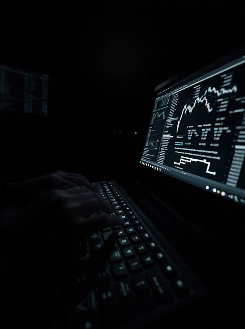 Hands typing on keyboard with financial graphs and data displayed on a dark computer screen.