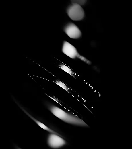 Close-up black and white image of a camera lens with visible focus and aperture markings.